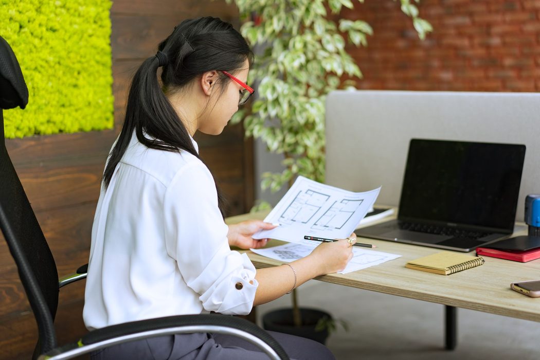 A person reviewing printed notes beside a laptop while comparing software options